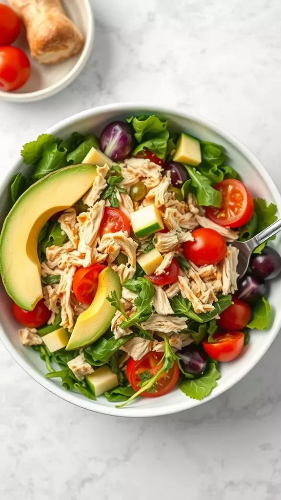 A bowl of shredded chicken salad with avocado, cherry tomatoes, and greens.